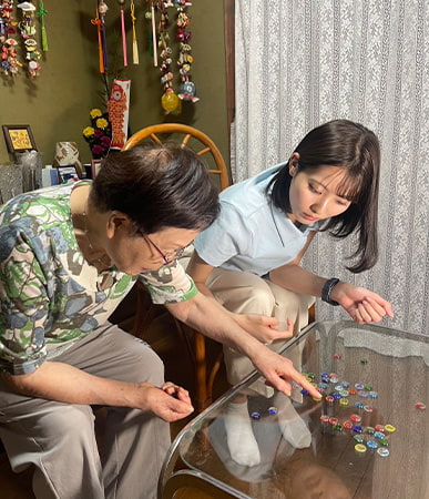 女性と共におはじき遊びを再現する山下七子